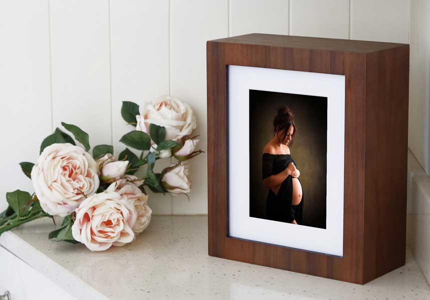 Crawley maternity portraits. A framed portrait of a pregnant woman cradling her belly occupies pride of place next to a bouquet of pale roses on a white countertop, capturing the essence of a thoughtful Baby Plan.