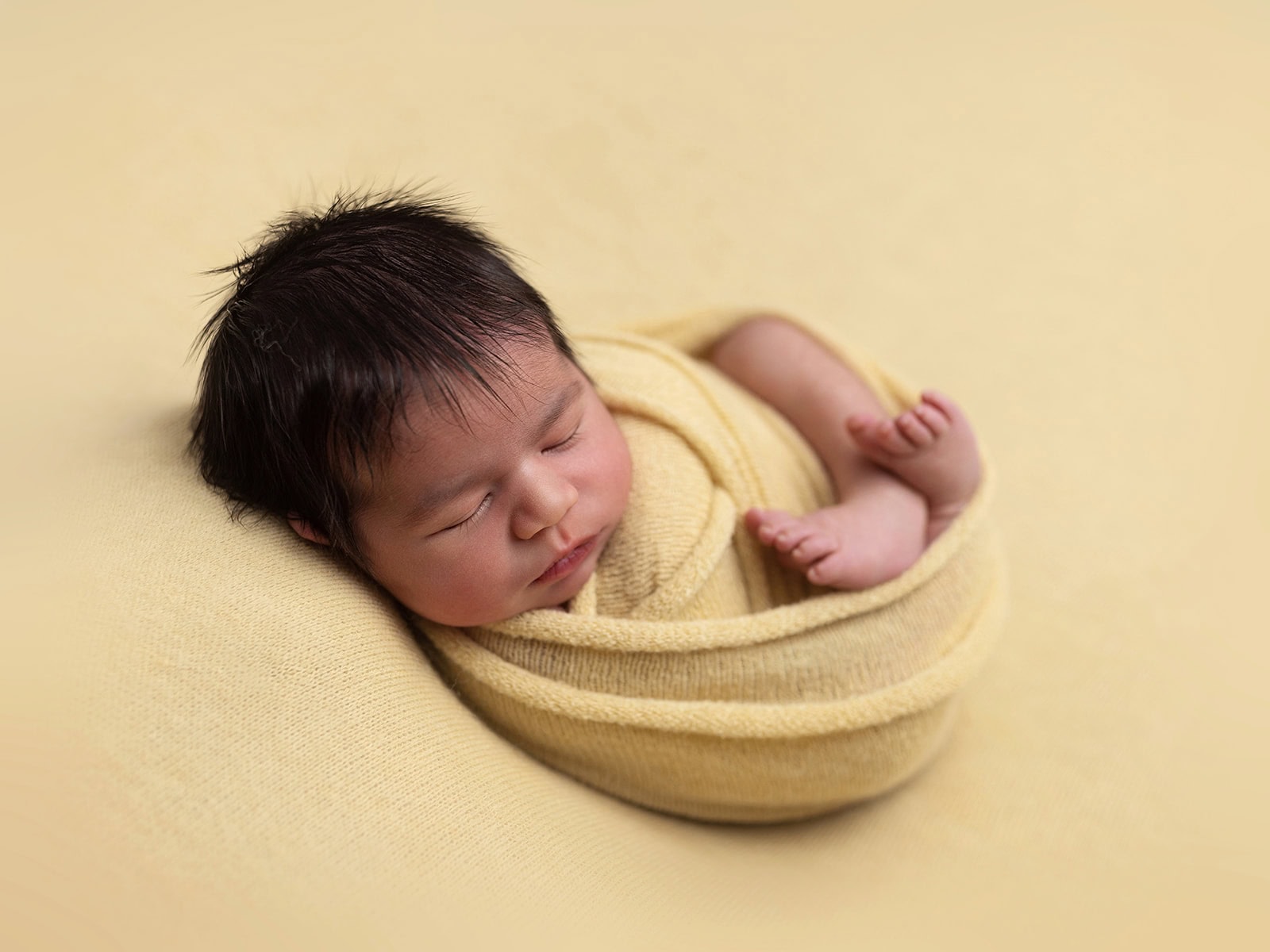 Newborn baby wrapped in a yellow blanket, peacefully sleeping on a matching yellow surface.
