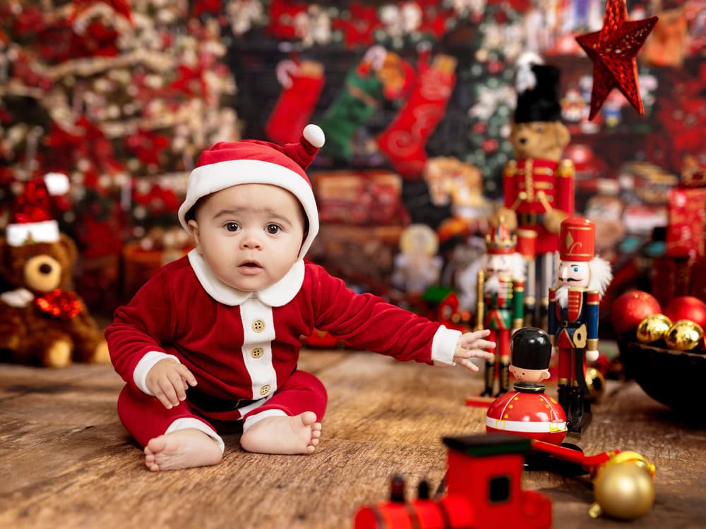 Baby in a Santa outfit sits on a wooden floor, surrounded by Christmas decorations and toys—perfect for capturing magical kids Christmas portraits or booking your Christmas mini sessions with a festive backdrop.