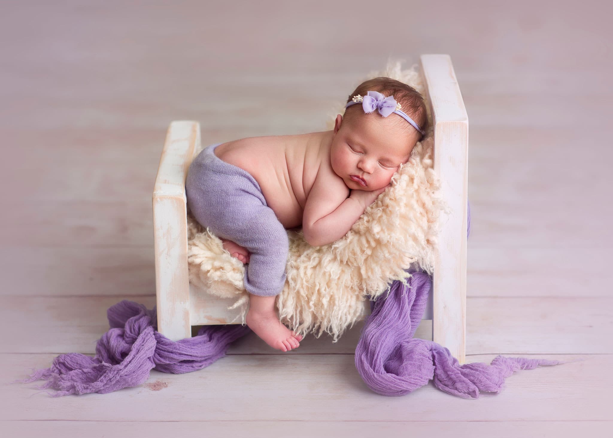 A newborn baby sleeps blissfully in a bespoke bed prop. Luxury newborn photography studio just a short drive from Lingfield, Surrey.