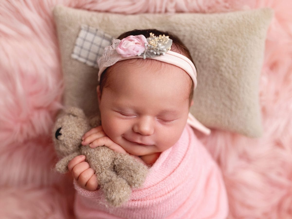 Professional baby-led newborn portraits for new parents in Merstham Surrey. Sleeping baby close-up, sleeping and smiling while holding a cute little teddy bear.