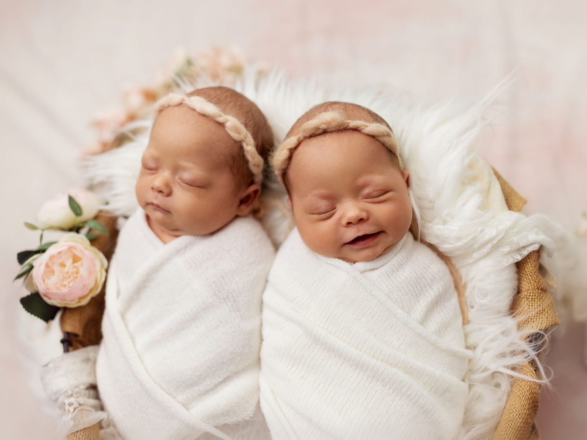 Twin baby girls photographed together in a cute bowl prop with floral accents. Newborn baby photography for parents in and around Redhill Surrey.