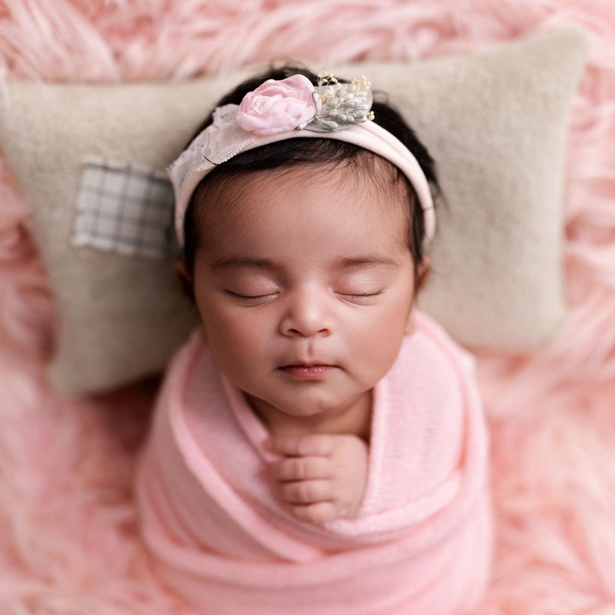 Award-winning baby photography for families in Crawley, featuring a newborn nestled in a luxury baby-pink wool wrap., with matching floral headband