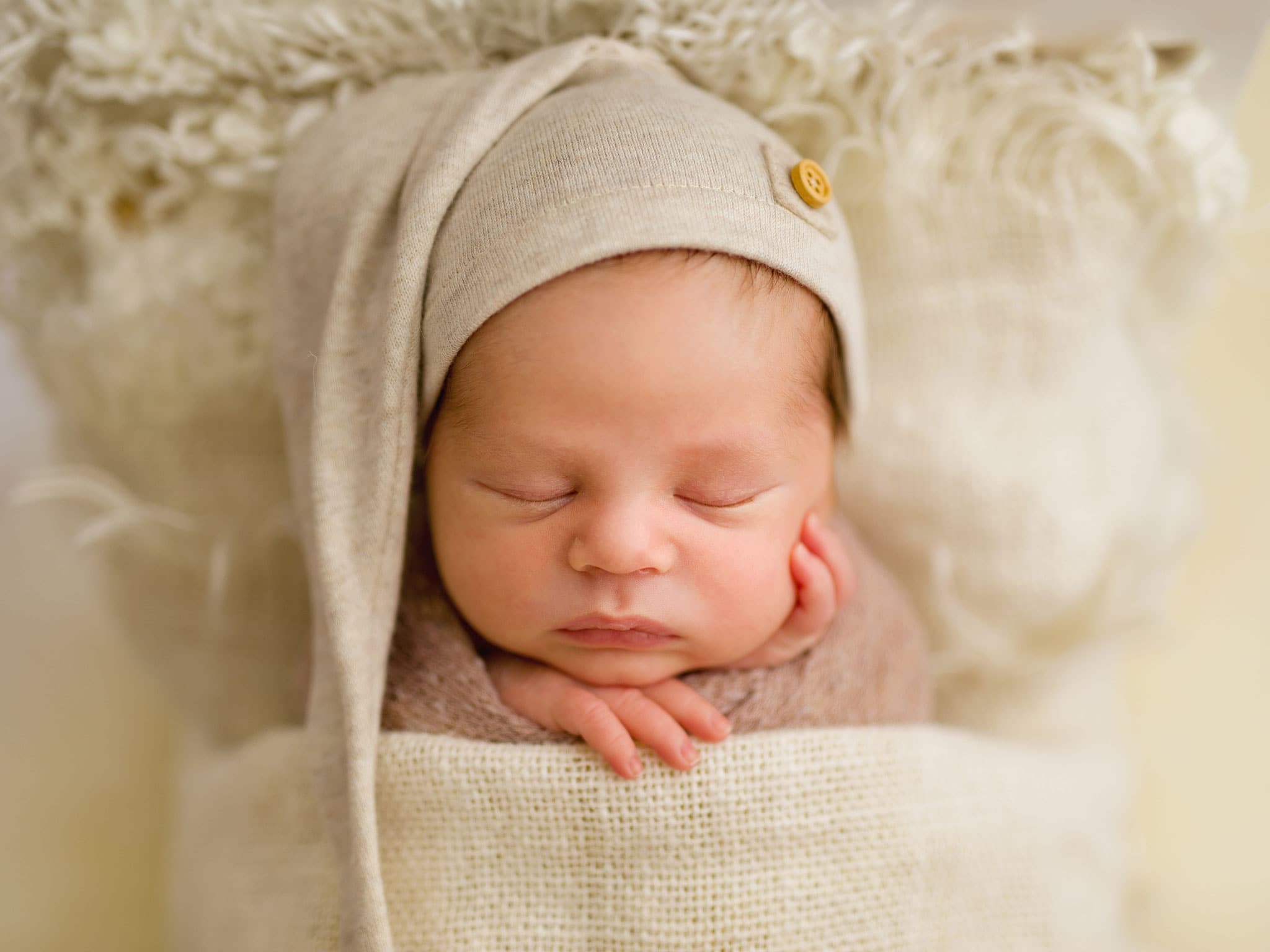Professional baby-led newborn portraits Merstham Surrey featuring close up baby portrait sleeping soundly on a soft wooden bed with hat.