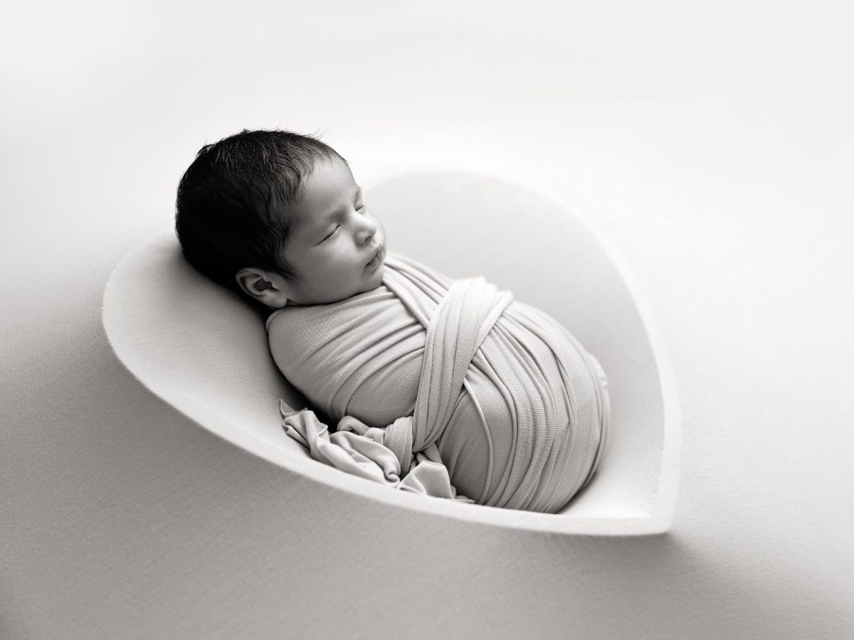 Professional baby photo session for families in Ansty and Haywards Heath, featuring a newborn in a beautiful heart-shaped bowl prop. This portrait is shot in black and white and backlit for simplicity.