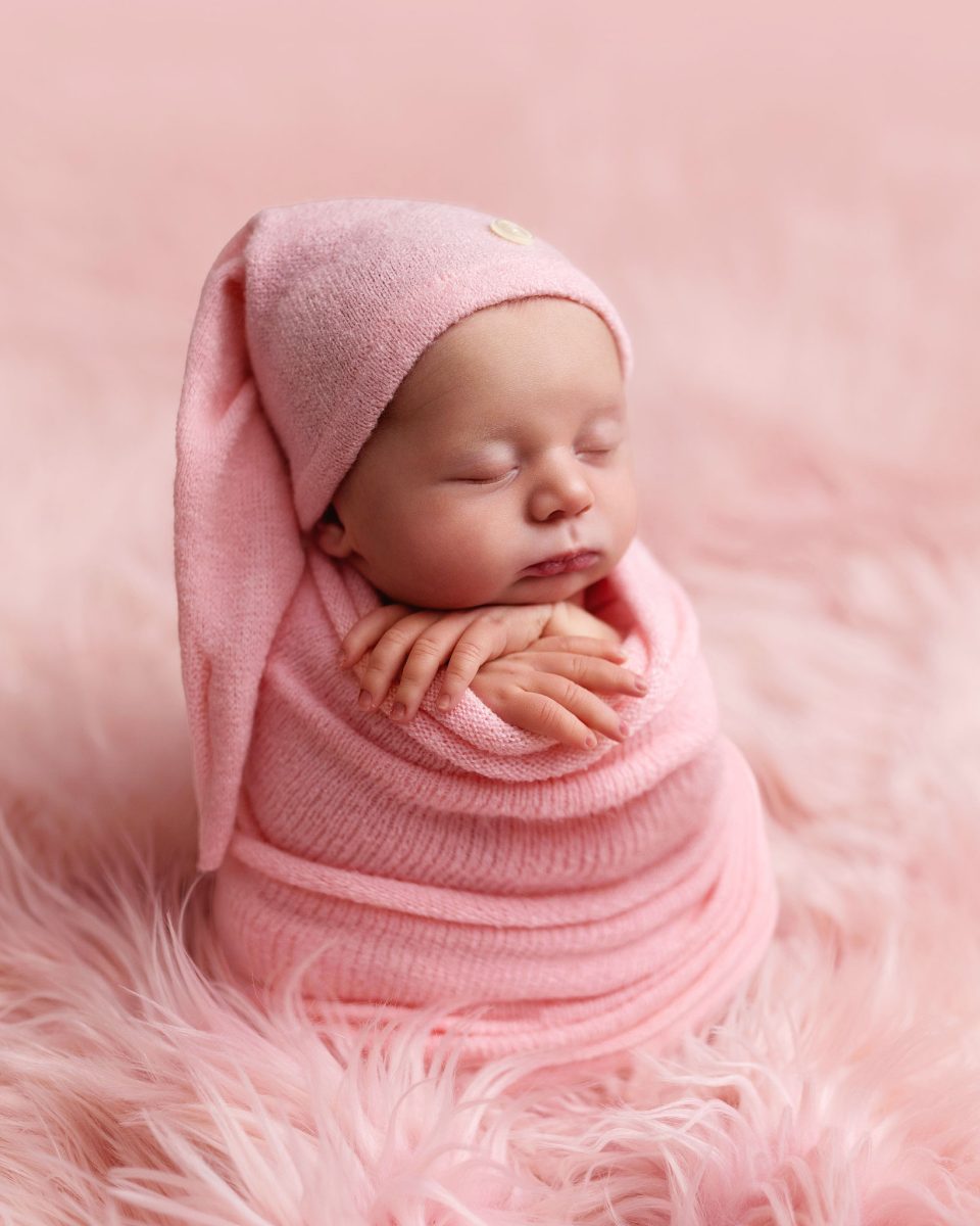 Professional baby photo session for families in Langshott, Horley, featuring a newborn in a n adorable pose with a soft pink wrap and matching bonnett.