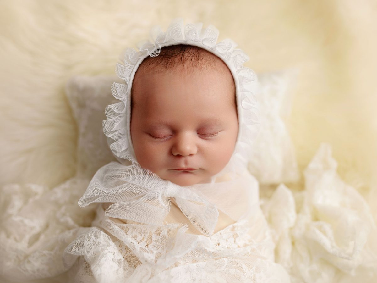 Professional baby photo session for families in West Hoathly and East Grinstead, featuring a newborn with a cream bonnet on a soft blanket in a wrap.