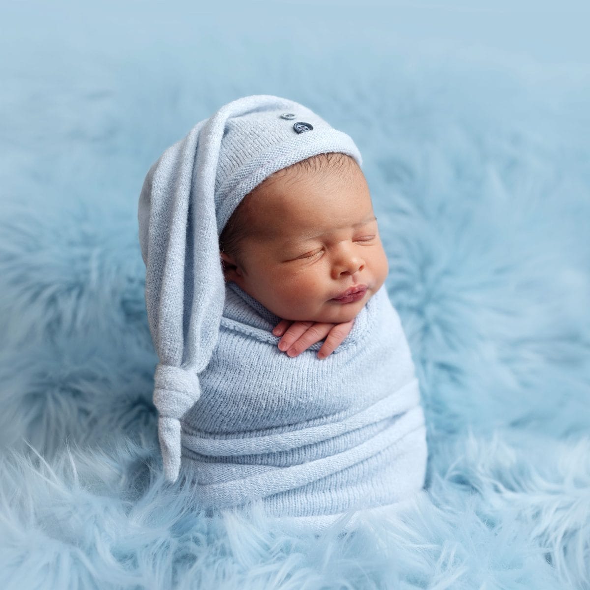 Baby photographer serving Staplefield and the Mid Sussex area, capturing a newborn baby in a potatoe sack pose, fully wrapped and snuggled in a warm wrap with cut woolly hat.