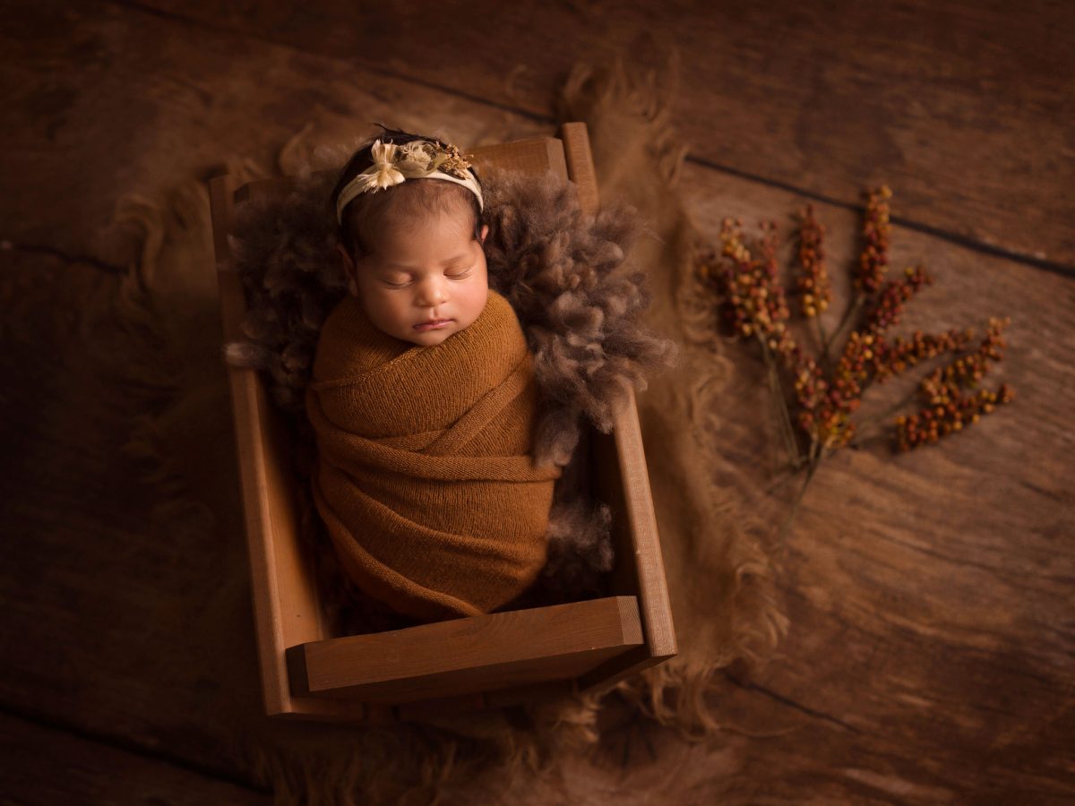 Baby photography services near Crawley town centre, featuring a sleeping newborn in a luxury wool posing bowl on a dark low-key background in fine art style.