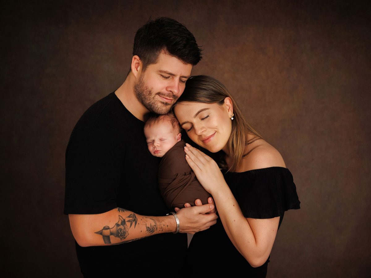 Baby photography services near Horsham town centre, featuring a sleeping newborn being held by both parents in a beautifully posed, low-key family newborn portrait.