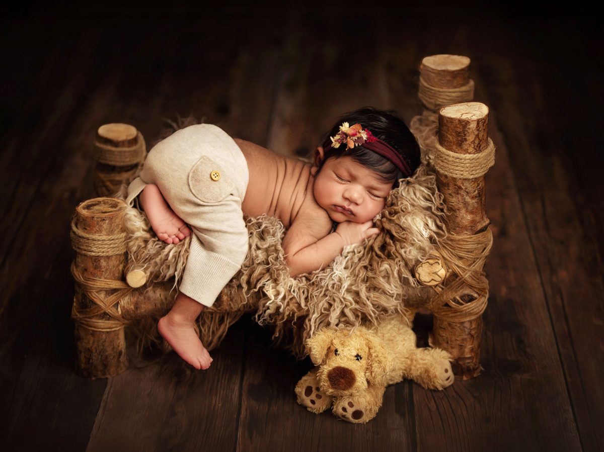 Burgess Hill maternity and newborn photography specialist: Stunning newborn portrait of a sleeping baby posed on a bespoke rustic bed with teddy bear and floral headband