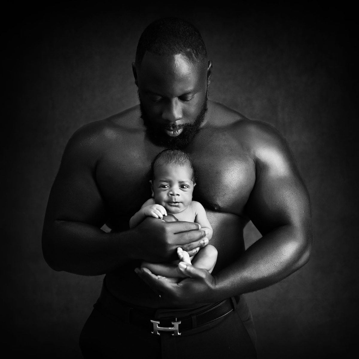 Fine Art baby photography in Horley featuring a strong Dad delicately holding his tiny new baby in his arms.