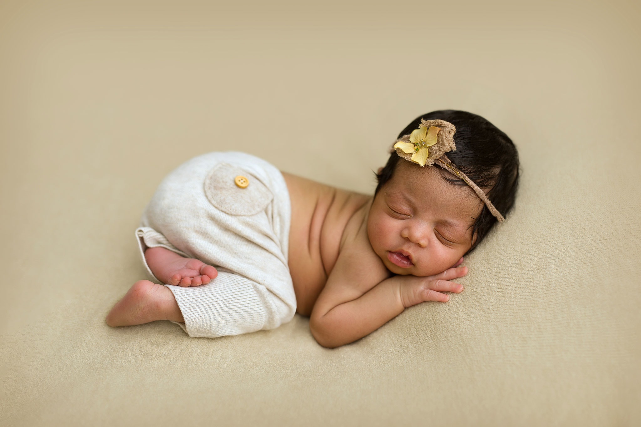 Fine art newborn photography near Nutfield and Bletchingley featuring an adorable baby sleeping in a very cute newborn pose on a soft beige blanket. Baby is wearing a matching outfit provided by the studio.
