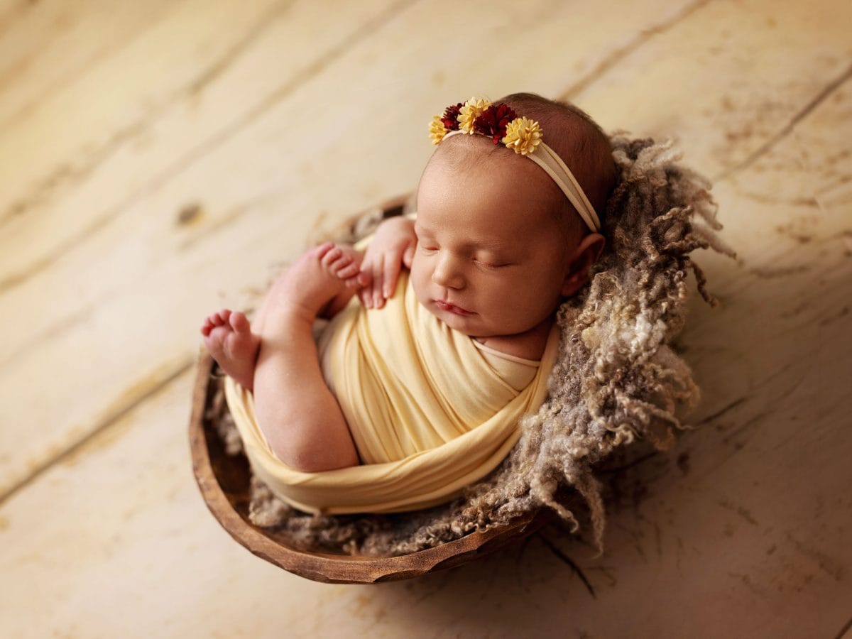 A newborn photoshoot featuring a baby wearing neutral tones while posed in a bespoke, rustic bowl for her first photoshoot near Lingfield, Surrey.