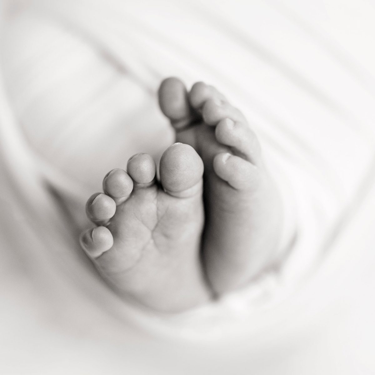 Newborn baby photos including detail shots for families in Hurstpierpoint and Burgess Hill. Fine art black and white image showing cute details of baby feet and toes in a soft, cushioned wrap.