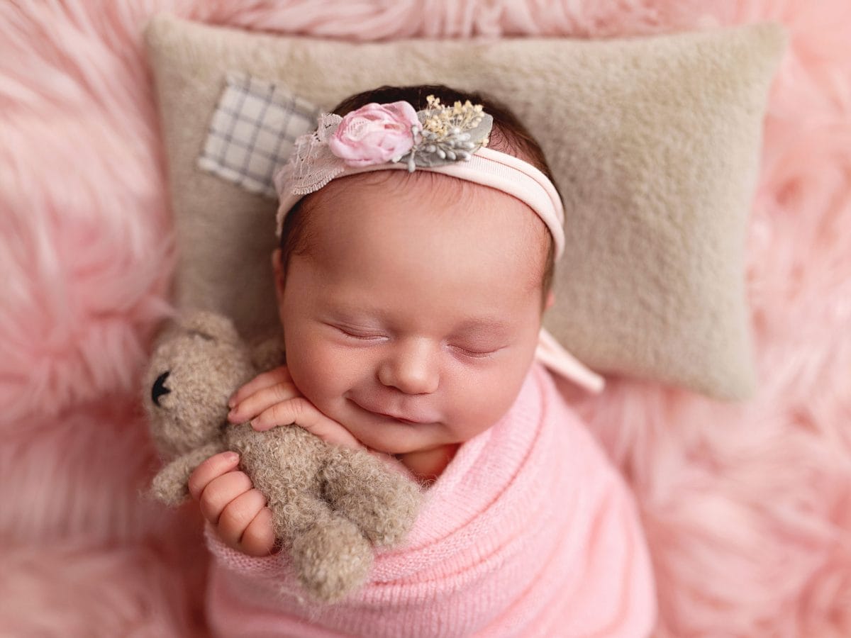 Newborn photographer serving Bewbush, Broadfield, and Crawley, showing a baby in a cozy, soft-knitted wrap clutching a tiny teddy bear and smiling.