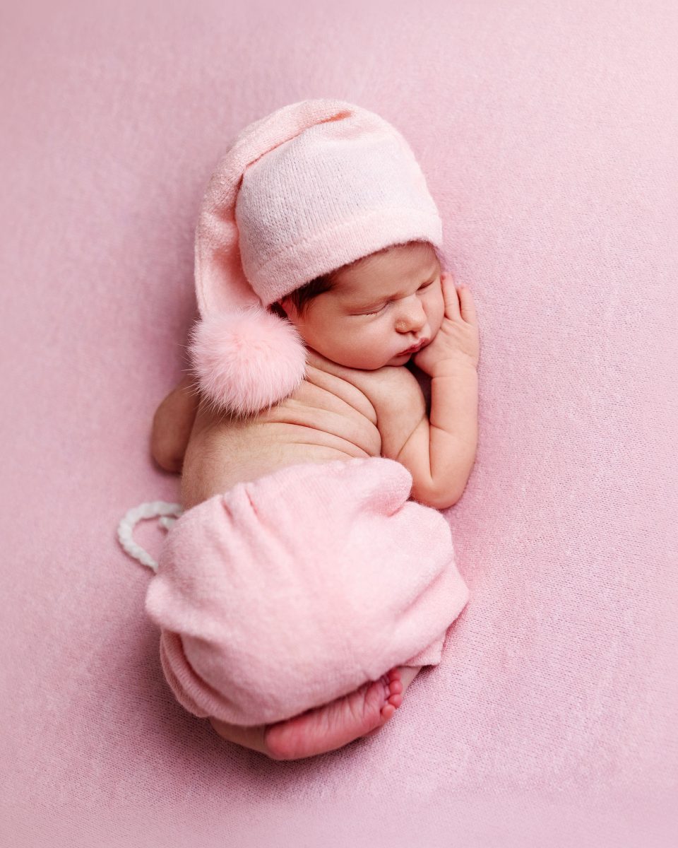 Natural newborn photographer serving families near Saint Hill, East Grinstead, showing a baby in a cozy, hand-knitted wrap with matching hat on a soft pink blanket.