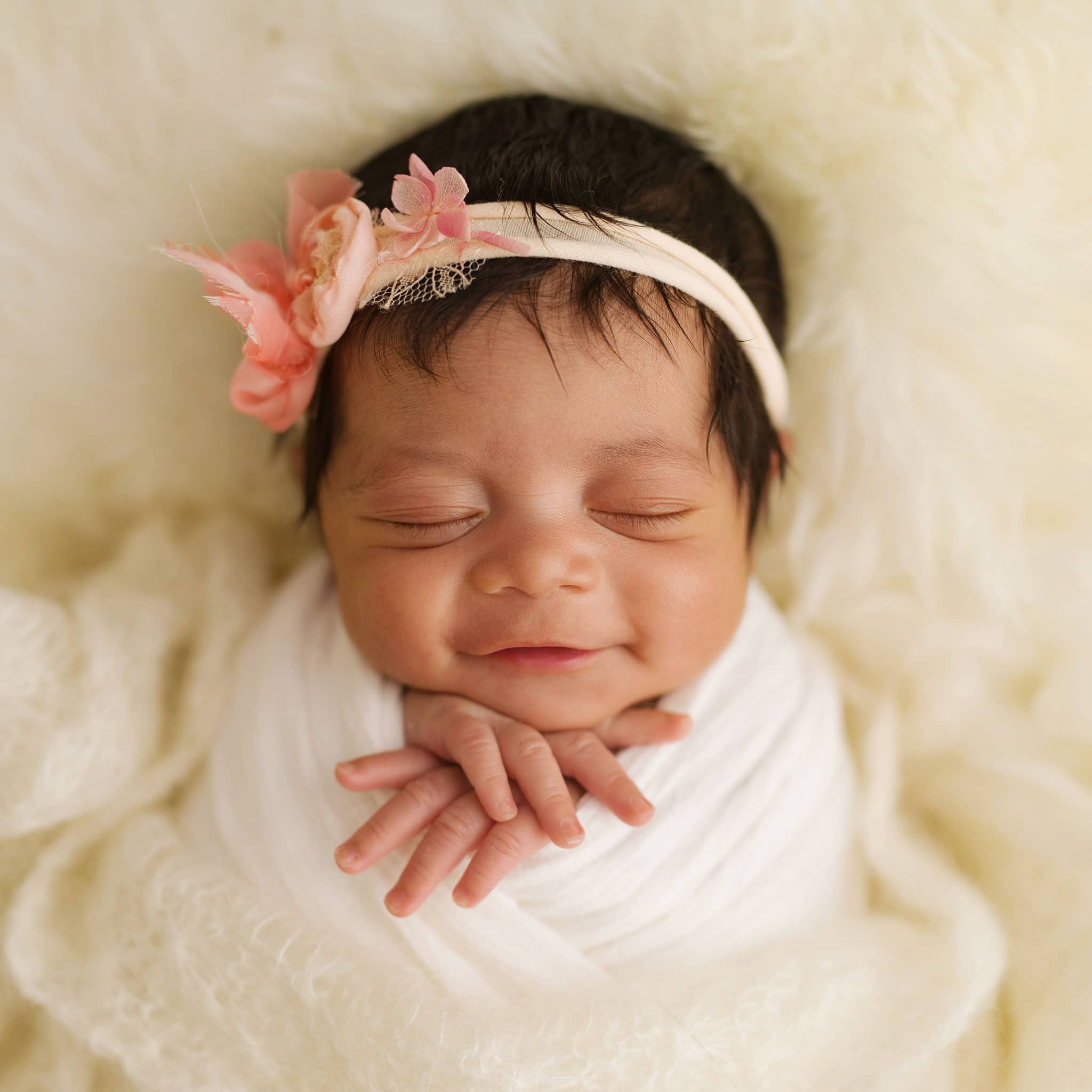 Professional newborn photographer West Sussex: A serene portrait of a sleepy smiling newborn baby girl in a pink floral headband.