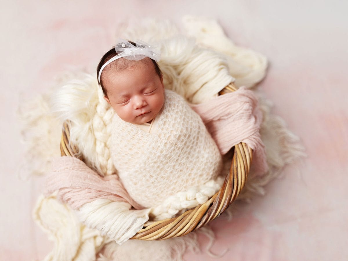 High-end newborn photography packages in the Haywards Heath area: A baby sleeping soundly in a wicker basket prop on a floral background in our studio.
