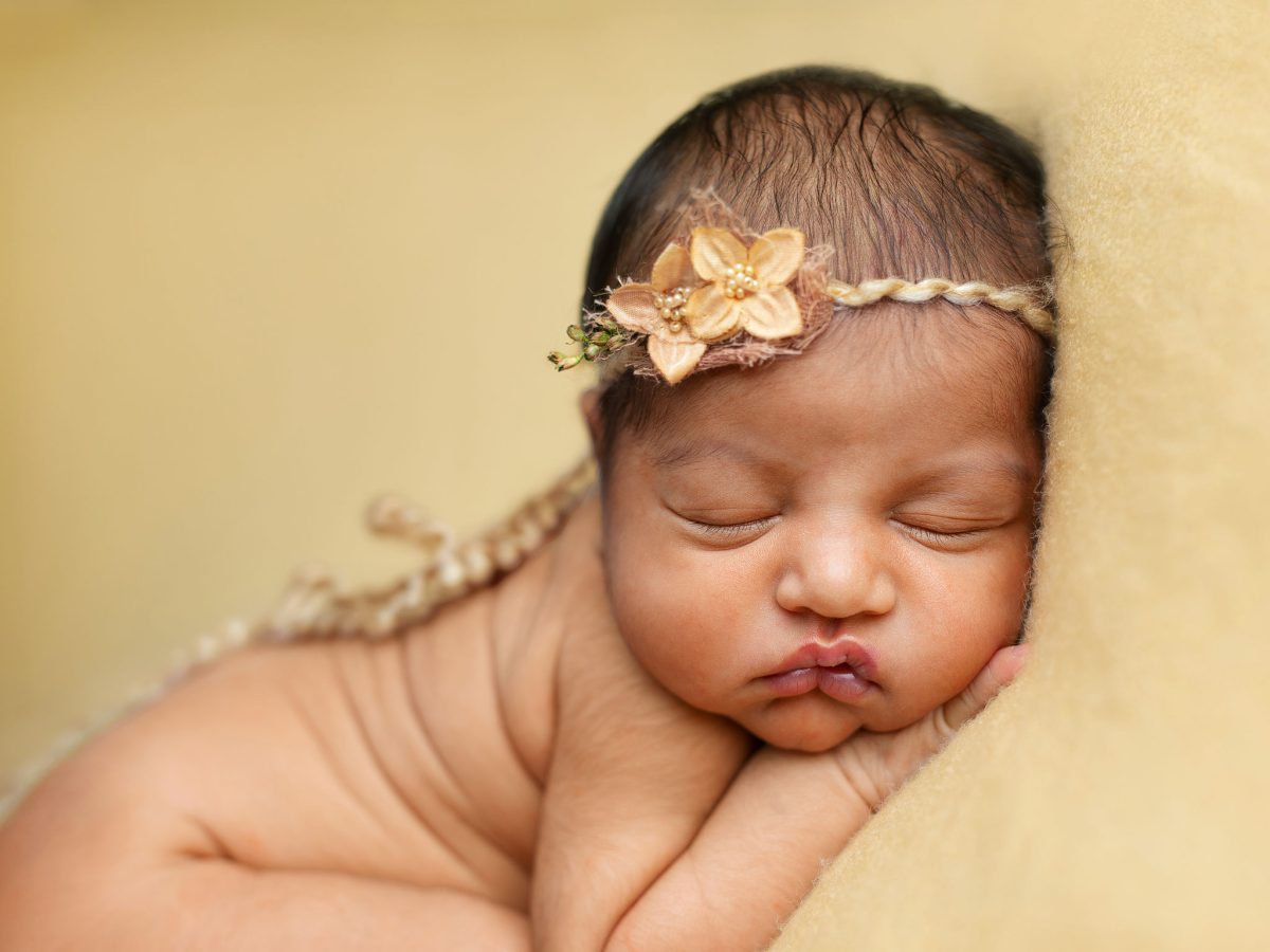Newborn photography for parents near Kings Weald, Burgess Hill. Beautiful close up portrait of baby face with floral headband, sleeping soundly on a soft mustard coloured blanket