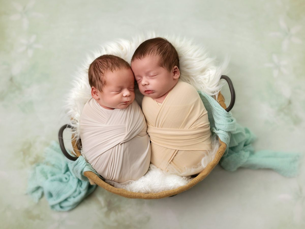 Newborn photoshoot with twins near Horley, featuring two babies sharing a large prop bowl on a sot green backdrop.