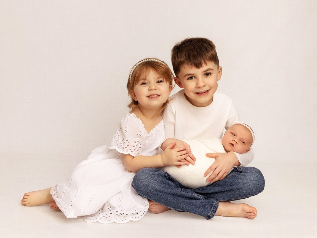 Sibling and newborn photos for Burgess Hill families, featuring a big brother and middle sister holding their new baby sister.