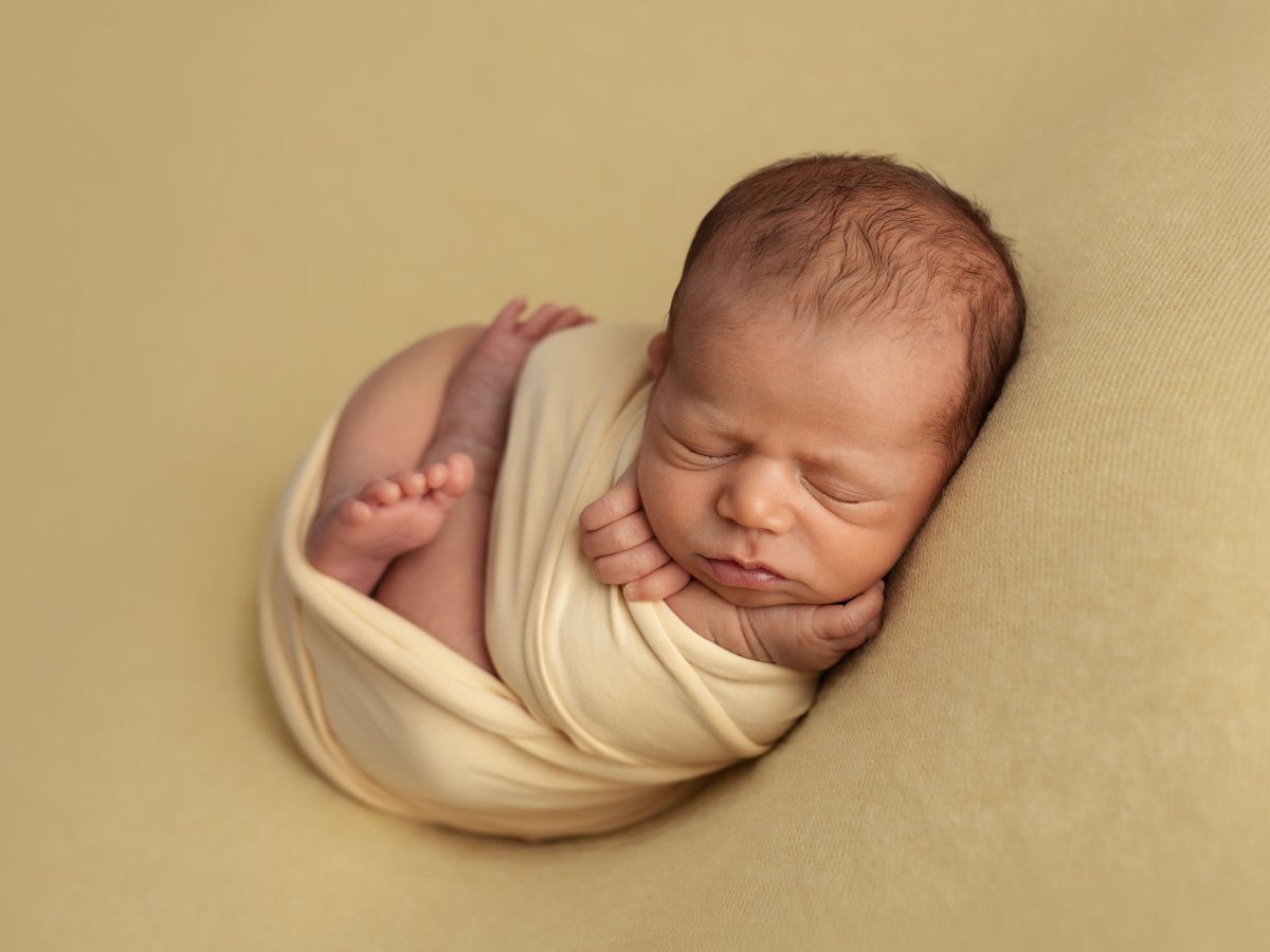 Top-rated newborn photographers serving Maidenbower. West Sussex. A peaceful baby sleeping in a snug, warm wrap on a soft blanket.