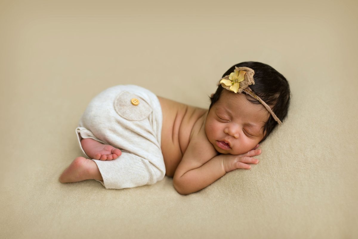 Top-rated newborn photographer in the RH17 Mid Sussex area: A very cute peaceful newborn baby in a classic studio setup, gently posed in a touchie pose with simple, matching headband and pants outfit.