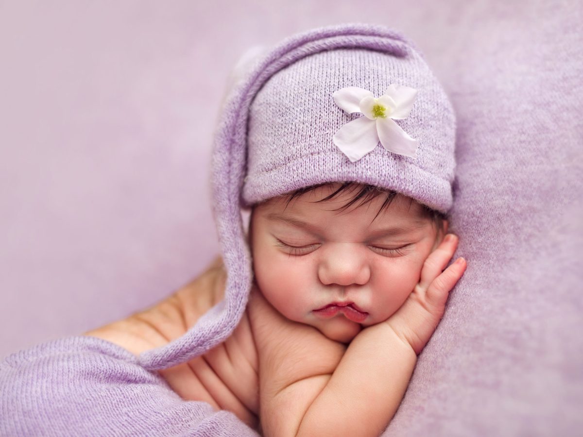 Top rated newborn photography for Sussex familes. Beautiful details of hands and fazce in this simple, naytural newborn portrait with purple hat and matching blanket setup.