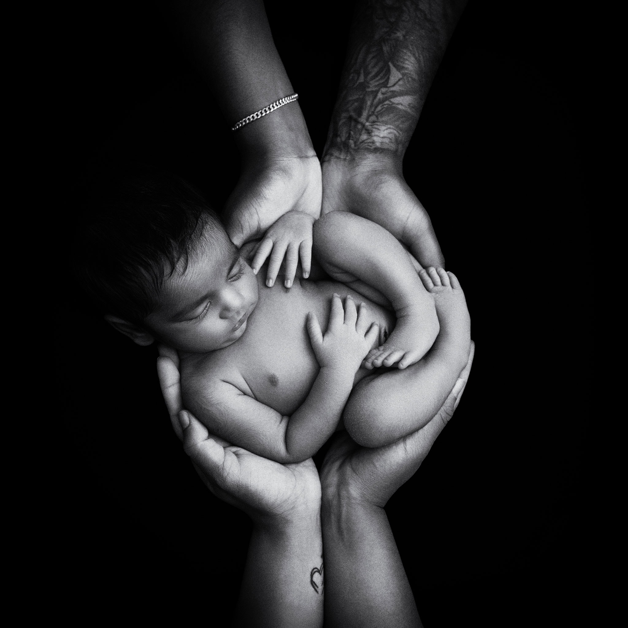 A newborn baby is safely and lovingly cradled in both parents hands for this fine-art style newborn portrait in black and white, with a textured finish applied during editing. Sussex newborn photography by Baby Shoots 